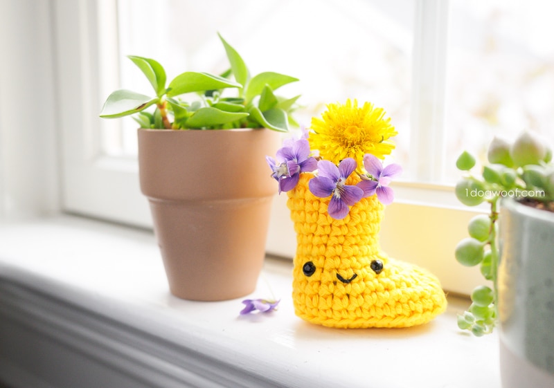 黄钩针雨鞋与紫色的花朵，坐在窗台